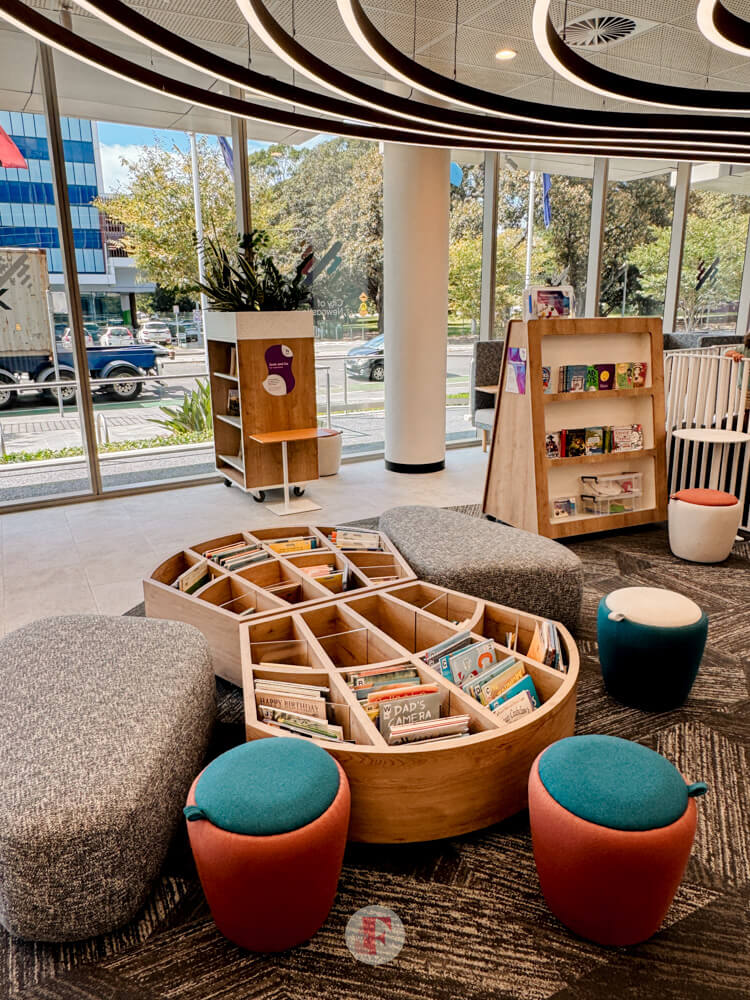 A picture of the children's book case centerpiece surrounded by a lounge area, book shelves, and glass walls