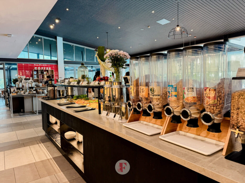 A breakfast buffet station at Rydges Hunter Valley featuring cereal dispensers and a variety of breakfast items, with a coffee bar visible in the background.