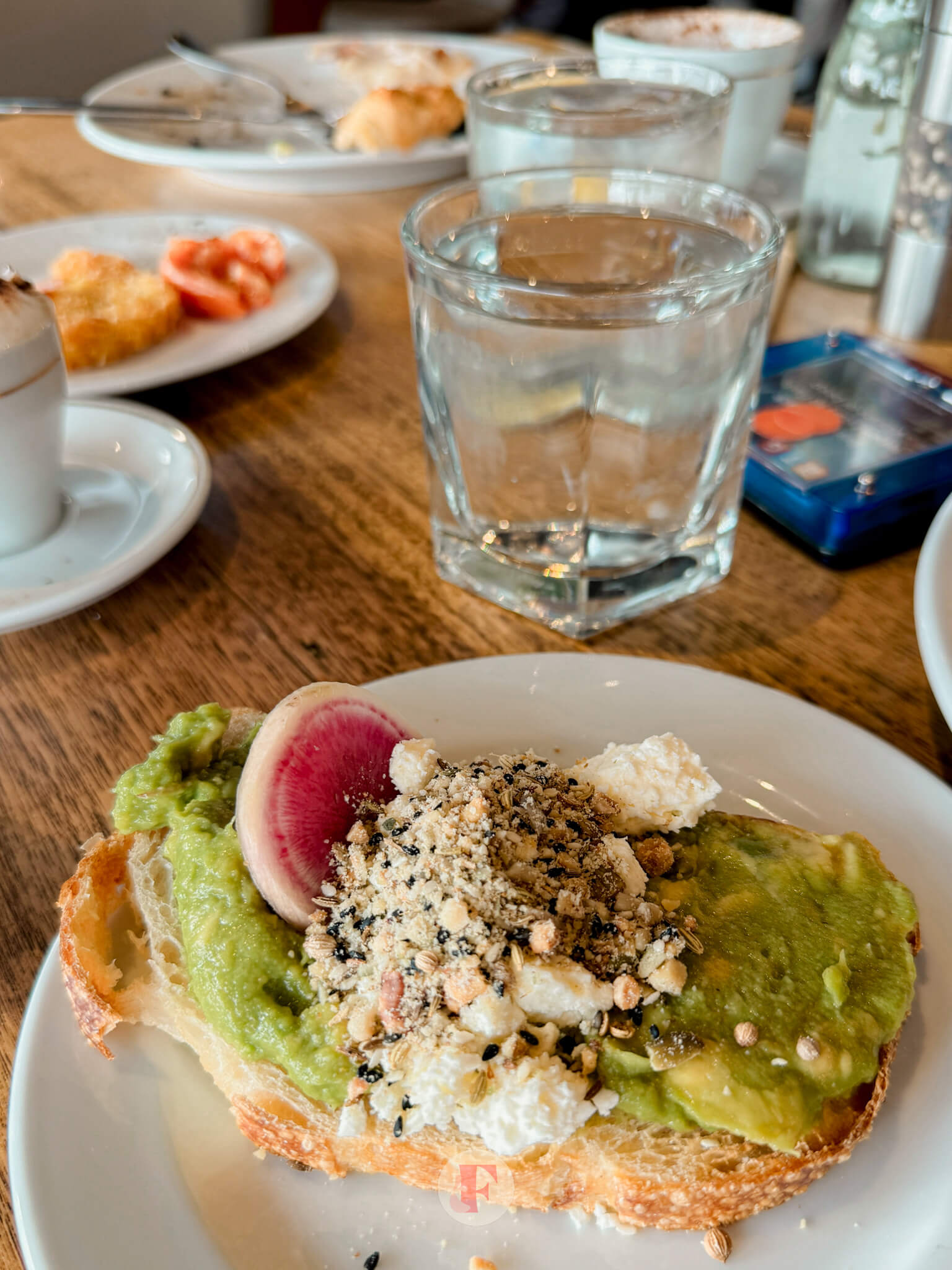 A close-up of an avocado toast with radish slices and crumbled cheese served on a rustic piece of bread at the Rydges Hunter Valley breakfast buffet.