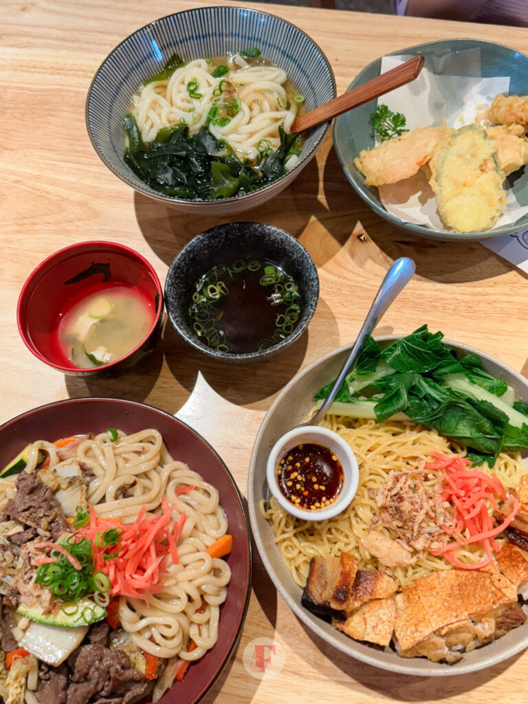 overhead shot of beef yakiudon, miso soup, pork crackling and dry noodle, and tempura with udon soup