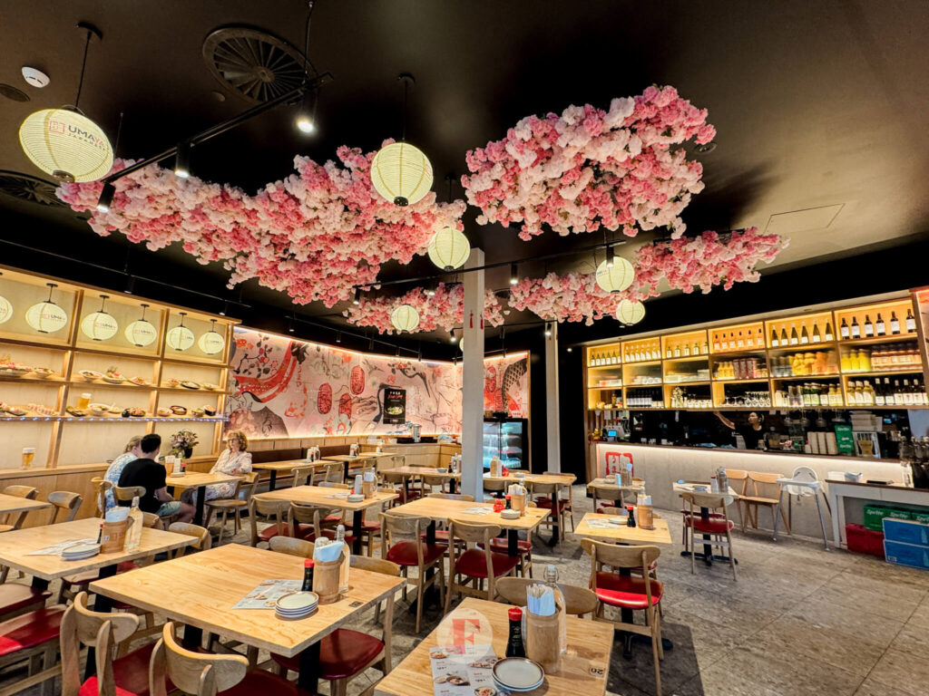 restaurant facade showing long tables and and open floor space and ceiling decor like cherry blossoms