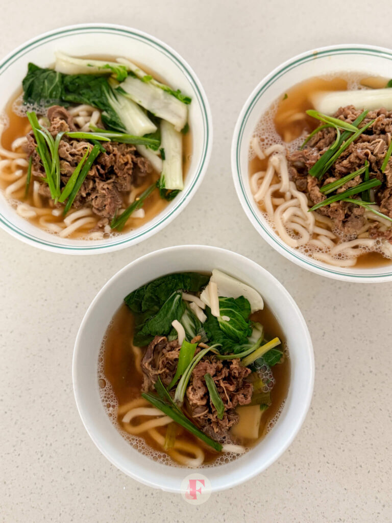 A top shot of a three bowls of beef udon soup with slices of green onions and bok choy on top