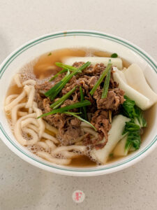 A top shot of a bowl of beef udon soup with slices of green onions and bok choy on top